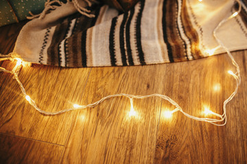 stylish golden garland lights on wooden floor at rug, preparation for winter christmas holidays. decor for winter holidays. atmospheric moment