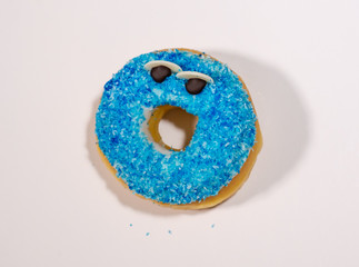 Top view studio photo of a delicious and tempting happy donut with blue sprinkles isolated on white background in unhealthy nutrition and sugar addiction concept.