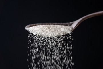 Studio picture of a metal spoon pouring sugar isolated on a black background in cooking sweet sugar addiction unhealthy diet overweight and obesity concept