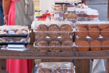 Cookies of different types in plastic containers on wooden rack sold at market. Handmade biscuits for sale.