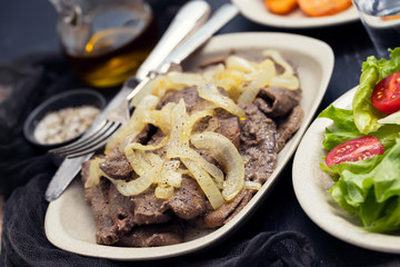 fried liver with onion on white dish and potato, salad