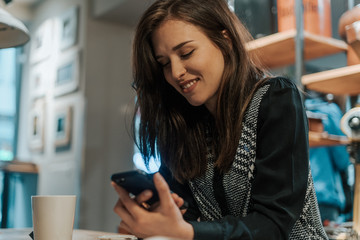 Beautiful young brunette looking at her phone in a coffee shop