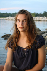 GIOVANE RAGAZZA IN POSA AL MARE DURANTE IL TRAMONTO 