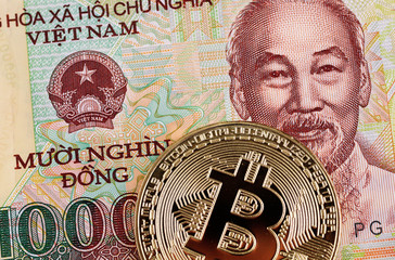 A macro image of a golden bitcoin against a 10000 Vietnamese dong note