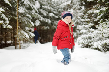 Fototapeta na wymiar Adorable little girl having fun in beautiful winter forest. Happy child playing in a snow.
