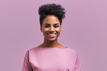 Happy African American businesswoman with positive smile, has crisp dark hair, rejoices having weekend and good rest after hard working exhausting week, isolated on lavender wall