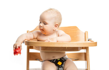 Cute baby girl going to drop tomato while sitting in high chair over white