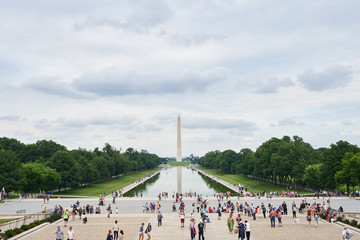 Crowds of tourists and people near reflecting pool in Washington D.C. with the Washington Monument in the background.