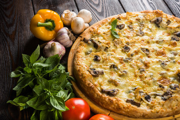 Pizza with mushrooms and cheese on a dark wooden background with fresh vegetables