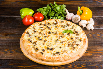 Pizza with mushrooms and cheese on a dark wooden background with fresh vegetables