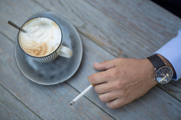 Closeup shot of a cup of coffee and a mans hand with a cigarette