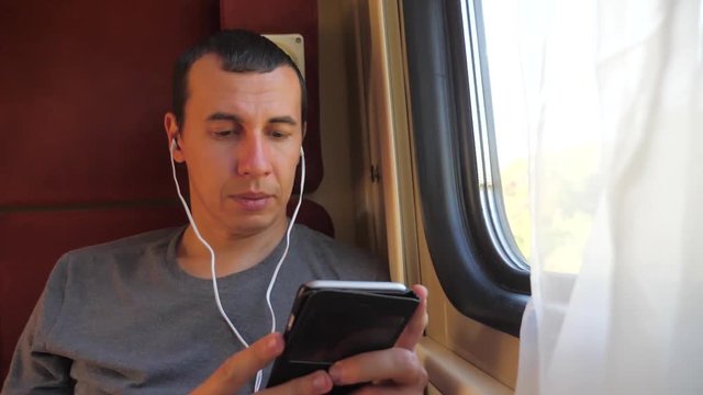 man listening to the music on the train rail car coupe compartment travel. slow motion video. man with a smartphone at the window of a train lifestyle in a car travel internet social media web. man