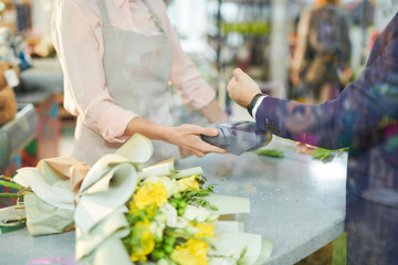 Mid section of modern gentleman paying via smartwatch while buying flowers in flower shop, copy space