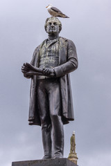 Glasgow, Scotland, UK - June 17, 2012: Closeup of  black bronze Robert Peel statue on stone pedestal at George Square against light blue sky. Plenty of Pigeon poop and one bird.