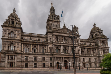 Fototapeta na wymiar Glasgow, Scotland, UK - June 17, 2012: Frontal view on Brown stone Glasgow City Chambers building aginst dark cloudscape. 
