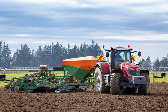 A farmer seeds his paddocks in the springtime using a pneumatic seed drill behind a red tractor