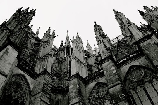 The monumental gothic-style Cologne Cathedral, Germany, stands up flaunting its typical ogival arches and needle pinnacles that rise and lengthen up high like wanting to reach the sky. Low angle, B&W.
