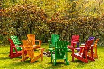 Wooden adirondack chairs arranged in a circle around a fire pit in the autumn colors.