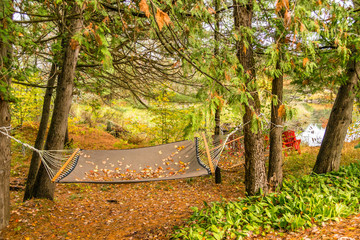 Fototapeta premium Cloth hammock set up in the autumn woods and looking at a slow moving river, cool weather, foliage in fall colors, wanderlust concept