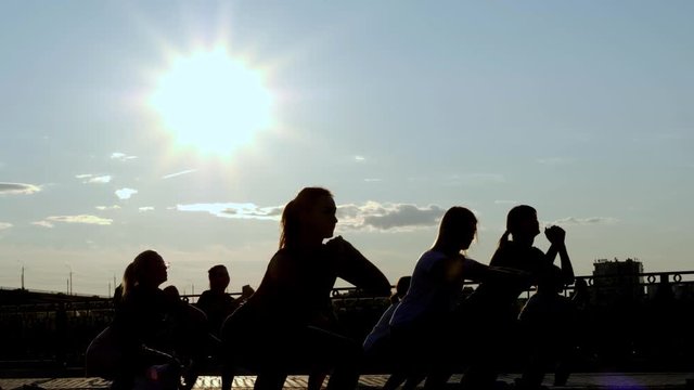 Silhouette of people doing yoga outdoor - Meditation and sport concept for healthy and relaxing lifestyle - group woman city training in park on sunset