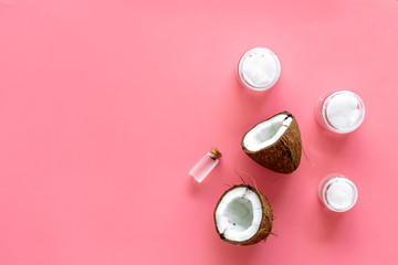 Fototapeta premium Cosmetics based on coconut oil. Oil in small bottle, cream, coconut pulp, half of coconut with shelf on pink background top view space for text