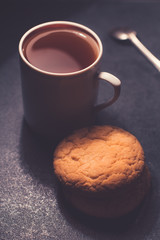 A glass cup of black tea with cookies. On a dark greyish marble background.