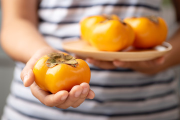 Hand holding persimmon fruit for giving, healthy eating
