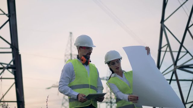 Power line workers looking at a scheme on paper. 4K.