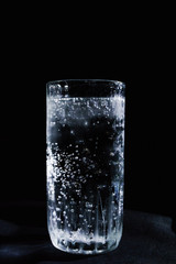 Soda water in glass on black backdrop with light on top