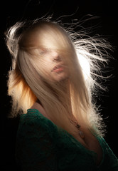 Beautiful blonde girl with flying hair in a green dress on a black background.