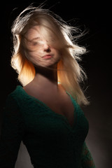 Naklejka premium Beautiful blonde girl with flying hair in a green dress on a black background.