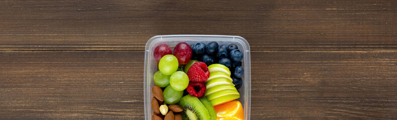Healthy fruits with almonds in takeaway box on wood banner background