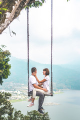 Young honeymoon couple swings in the jungle near the lake, Bali island, Indonesia.