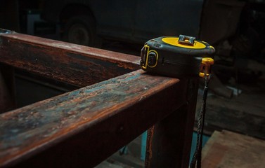 yellow measuring tape lies on a rusty metal product on a dark background