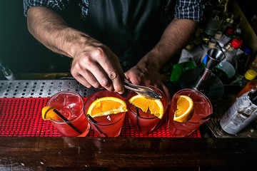 hands of the bartender who prepares red cocktails with orange slices, top view