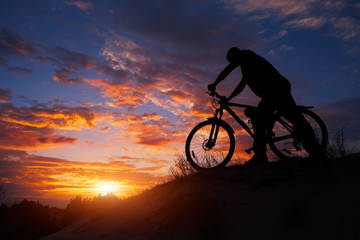 Fototapeta na wymiar Silhouette of sports person cycling on the meadow on the beautiful sunset. Young man riding bicycle.