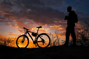 Fototapeta premium Silhouette of sports person cycling on the meadow on the beautiful sunset. Young man with camera and bicycle.