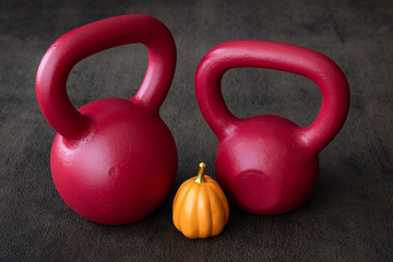 Naklejka na ściany i meble Two red kettlebells on a brown leather textured background, with an orange ceramic pumpkin 