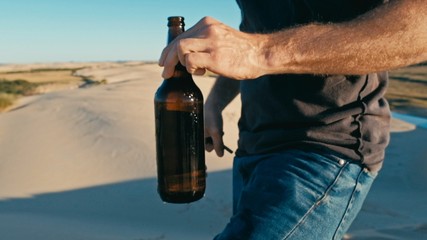 young man opening a bottle of beer outdoor in the desert sand dunes