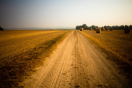 Petite route de sable rurale étirée vers l'horizon et bordée de balles de foin sur la droite