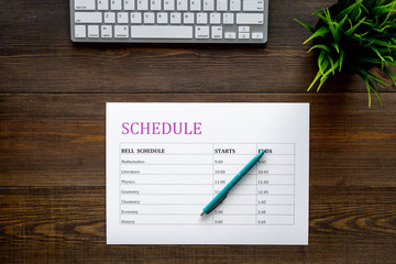 School student's schedule with time of lessons on dark wooden office desk with computer keyboard top view copy space