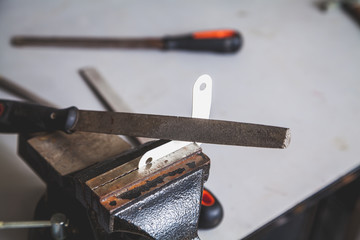 Metal corner clamped in bench screw. Above is file