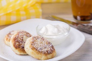 Tasty cottage cheese pancakes with  sour cream and powdered sugar in a white plate.  Homemade pastries