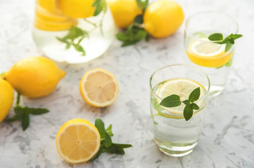 Refreshing lemonade with lemons, mint in a transparent jug and glasses on a light concrete background close-up. Background and place for text, inscriptions