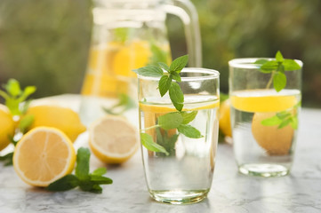 Refreshing lemonade with lemons, mint in a transparent jug and glasses on a light concrete background close-up. Background and place for text, inscriptions