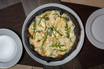 Black four cheese pizza served on the table in restaurant. Quattro formaggi pizza with pears on black dough top view