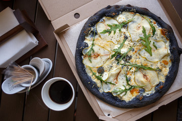 Take away Black pizza four cheese with coffee top view image in cafe. Quattro formaggi pizza with pears in pizzeria