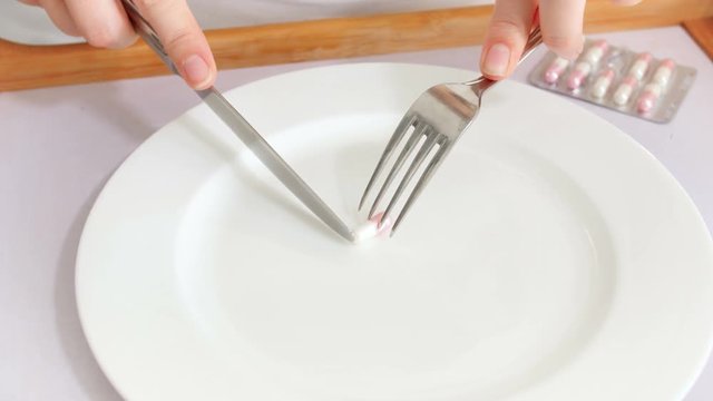 Conceptual 4k footage of pills for loosing weight. Female hands eating medicaments for weight loss with fork and knife