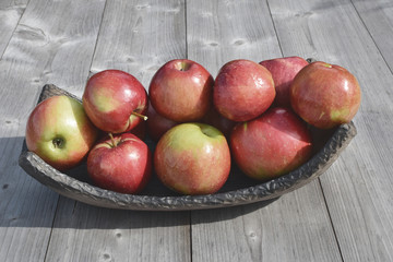 Red shiny apples in pottery dish on grey natural wooden background with copy space for text vintage tone style.  Freshly harvested sweet tasty fruit as healthy snack or for preparing salad cooking or 