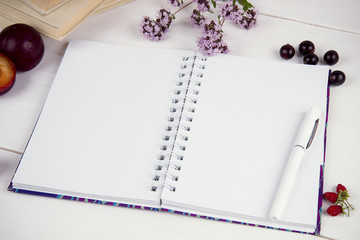 open notebook with clean sheets on a white table and flowers of oregano.